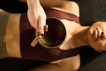 Fototapeta na wymiar High angle view of young woman using singing bowl in yoga practice together with instructor