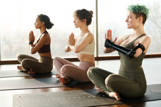 Group of young girls sitting in lotus position with eyes closed and meditating together in class