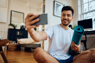 Happy sportsman taking selfie with cell phone while exercising in living room.