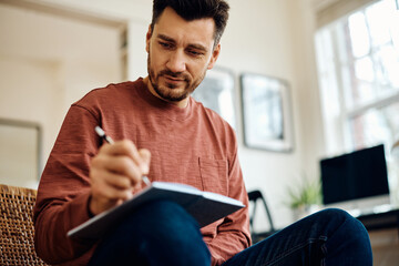 Smiling man writing in notebook in living room.