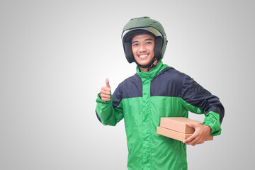 Portrait of Asian online courier driver wearing green jacket and helmet delivering package and box and showing thumb up hand gesture. Isolated image on white background