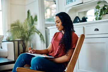 Young African American woman writes diary while relaxing at home. - obrazy, fototapety, plakaty