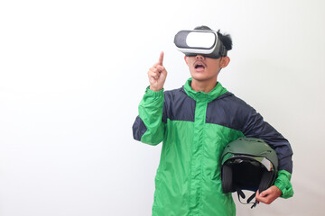 Portrait of Asian online taxi driver wearing green jacket and holding a helmet while using virtual reality or VR and pointing. Isolated image on white background