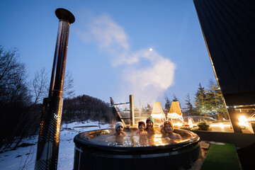 Family enjoying bathing in wooden barrel hot tub in the terrace of the cottage. Scandinavian...