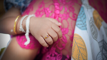 A baby's right hand wearing gold bracelet and two thick white yarn bracelets, and a gold ring on his finger. 