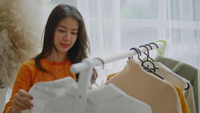 Home wardrobe or clothing shop changing room.Beautiful attractive young Asian woman choosing her fashion outfit clothes in closet living room at house or store.female think what to wear casual shirt.