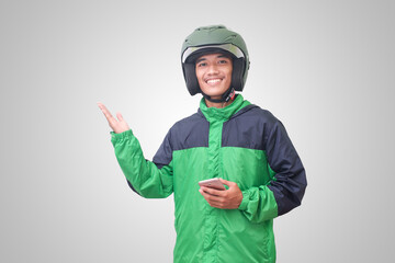 Portrait of Asian online taxi driver wearing green jacket and helmet holding mobile phone and pointing to empty space with finger. Isolated image on white background