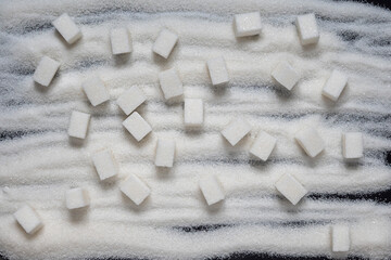 Lump sugar, refined, lies on the scattered granulated sugar