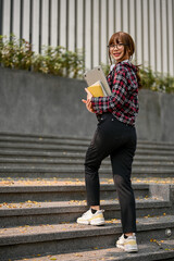 Charming Asian female college student walking up the stairs outside the campus building