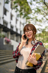 Asian female college student talking on the phone while standing outside of the campus building.
