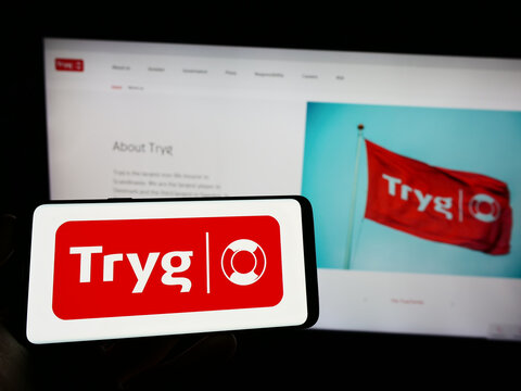Stuttgart, Germany - 03-12-2023: Person holding mobile phone with logo of Danish insurance company Tryg Forsikring AS on screen in front of web page. Focus on phone display.