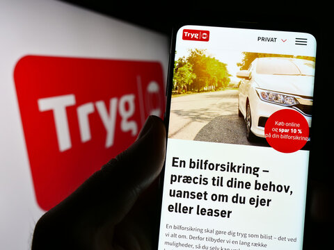 Stuttgart, Germany - 03-12-2023: Person holding cellphone with website of Danish insurance company Tryg Forsikring AS on screen in front of logo. Focus on center of phone display.