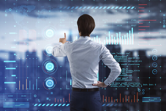 Back view of young businessman using glowing digital interface with business charts and coding on blurry city background. Future and cyberspace concept. Double exposure.
