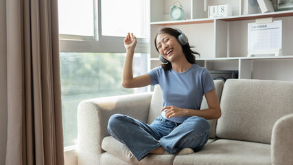 Young Asian woman happily listening to music through headphones, Woman was enjoying listening to her favorite music and rocking to the beat of the music, Stress relief, Happiness in life.