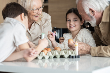 Little girl smiling and looking at the camera while decorating Easter eggs with her family