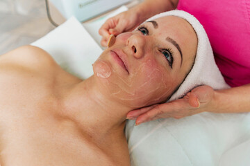 Cosmetologist applying hydrating mask on client's face in spa salon for better skin