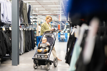 Casualy dressed mother choosing sporty shoes and clothes products in sports department of...