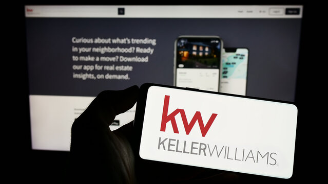 Stuttgart, Germany - 03-13-2023: Person holding cellphone with logo of US real estate company Keller Williams Realty Inc. on screen in front of webpage. Focus on phone display.