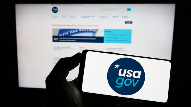 Stuttgart, Germany - 03-13-2023: Person holding cellphone with logo of US federal government website USA.gov on screen in front of webpage. Focus on phone display.