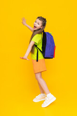 A little girl with a school backpack. A child in summer shorts is going to educational courses. Additional classes. A full-length schoolgirl on a yellow isolated background.