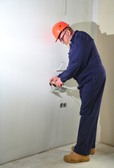 Professional electrician technician installing a wall socket in a new house. Electrical repairs at home. Electrician mounting wiring for electric sockets.