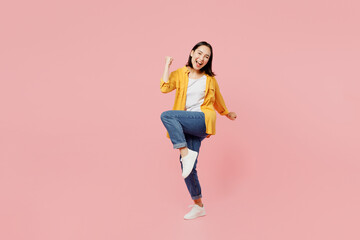 Full body excited young woman of Asian ethnicity wear yellow shirt white t-shirt doing winner gesture celebrate clenching fists say yes isolated on plain pastel light pink background studio portrait.
