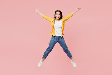 Fototapeta na wymiar Full body side view happy excited young woman of Asian ethnicity wear yellow shirt white t-shirt jump high with outstretched hands legs isolated on plain pastel light pink background studio portrait.
