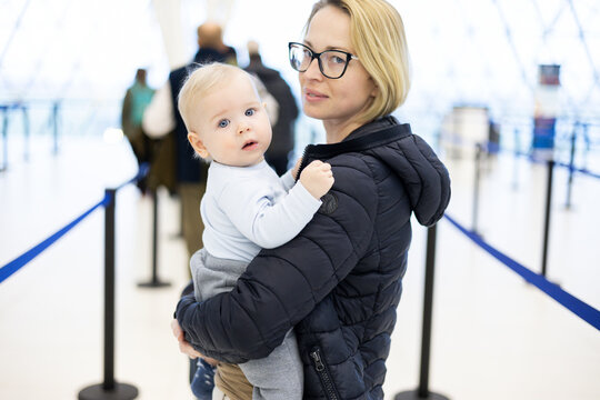 Mother holding his infant baby boy child queuing at airport terminal in passport control line at immigrations departure before moving to boarding gates to board an airplane. Travel with baby concept.