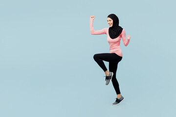 Fototapeta na wymiar Full body winner young asian muslim fitness trainer sporty woman wear pink abaya hijab spend time in home gym running in place isolated on plain blue background studio. Workout sport fit abs concept.