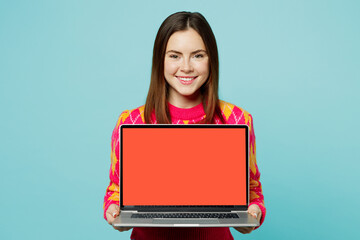 Naklejka premium Young smiling fun cheerful student IT woman wear bright casual clothes hold use work on laptop pc computer with blank screen workspace area isolated on plain pastel light blue cyan background studio
