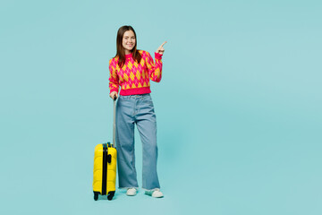 Traveler happy woman wear casual clothes hold suitcase point aside isolated on plain blue cyan background studio Tourist travel abroad in free spare time rest getaway Air flight trip journey concept.