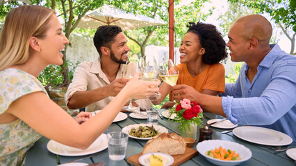 Group Of Friends Enjoying Outdoor Meal And Wine On Visit To Vineyard Restaurant With Cheers