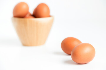 Several fresh chicken eggs placed in and out of a bamboo container on a white background. Foreground in focus and background blurred. Copy space.