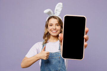 Young fun woman wearing casual clothes bunny rabbit ears hold use use mobile cell phone with blank screen area show thumb up isolated on plain pastel purple background. Lifestyle Happy Easter concept.