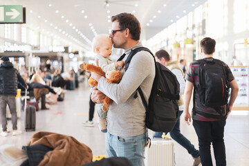 Father traveling with child, holding and kissing his infant baby boy at airport terminal waiting to...