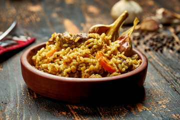 Classic pilaf with beef, garlic and carrots in a clay plate on a wooden background. Rustic