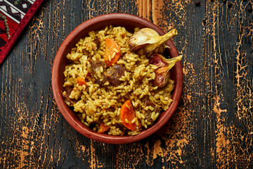 Classic pilaf with beef, garlic and carrots in a clay plate on a wooden background. Rustic