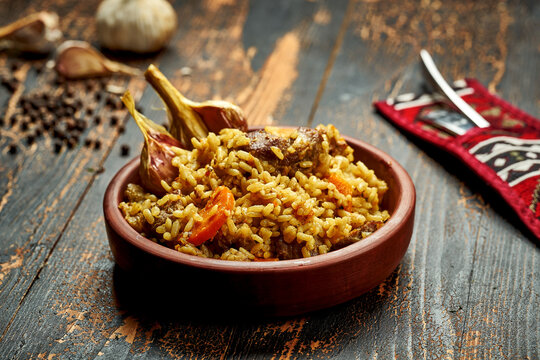 Classic pilaf with beef, garlic and carrots in a clay plate on a wooden background. Rustic