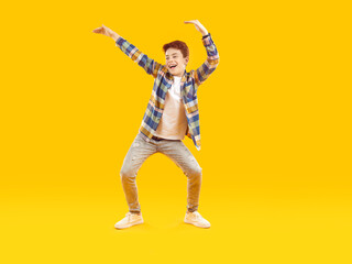 Happy dancing child. Full body shot of a funny kid dancing against a yellow studio background. Full length portrait of a cheerful, carefree school boy in casual clothes dancing and having fun