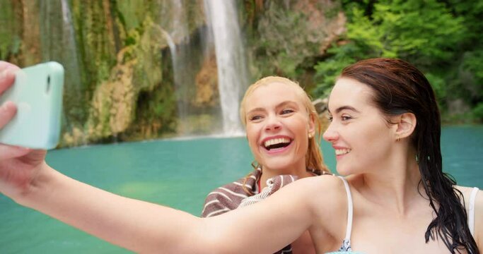 Phone selfie, waterfall and women in river, a swim on summer adventure in water. Friendship, freedom and travel, happy friends on vacation swimming in tropical lake and taking picture in natural pool