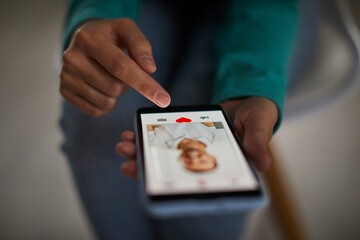 Close up of african american woman's hands putting red heart button giving like to a man's photo on her mobile dating application. Find love and online dating concept. Selective focus.