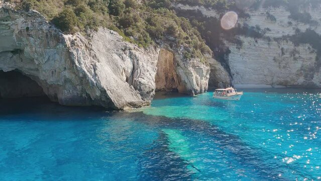 Anchored sailboats in turquise blue by near large sea caves in paxos island greece, slow motion