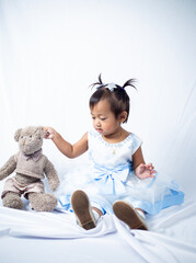 A little 2 year old southeast asian girl sitting down with her teddy bear on white background. 