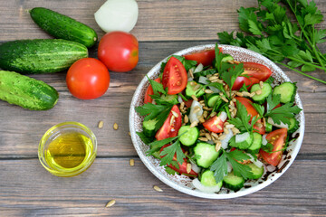 A bowl of tomato and cucumber salad with olive oil and parsley on wooden table