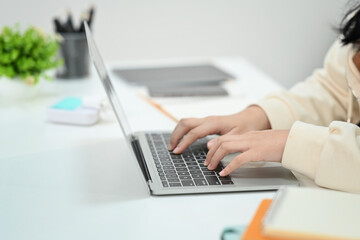 Close up view of female employee hands typing on laptop compute keyboard, searching online information working at office desk