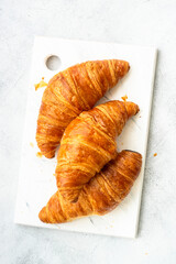 Fresh Croissants on cutting board at white table. Fresh bakery. Top view image.