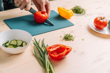 Lady cutting tomato for vegetable salad with microgreens.