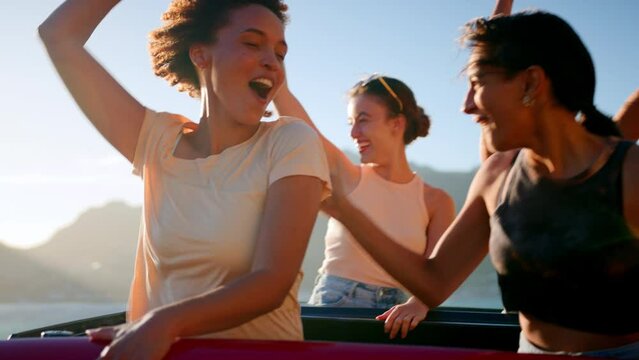Portrait of female friends standing up through sunroof of car laughing on road trip through countryside with friends - shot in slow motion