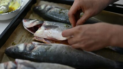 Closeup view of woman putting spices on sea bass fish before putting into oven