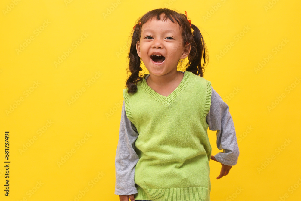 Wall mural Attractive Asian little girl smiling to the camera isolated on yellow background. 